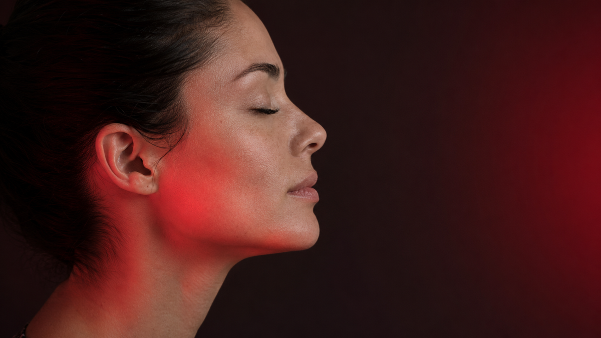 Side-profile portrait in soft red light illustrating facial device technologies