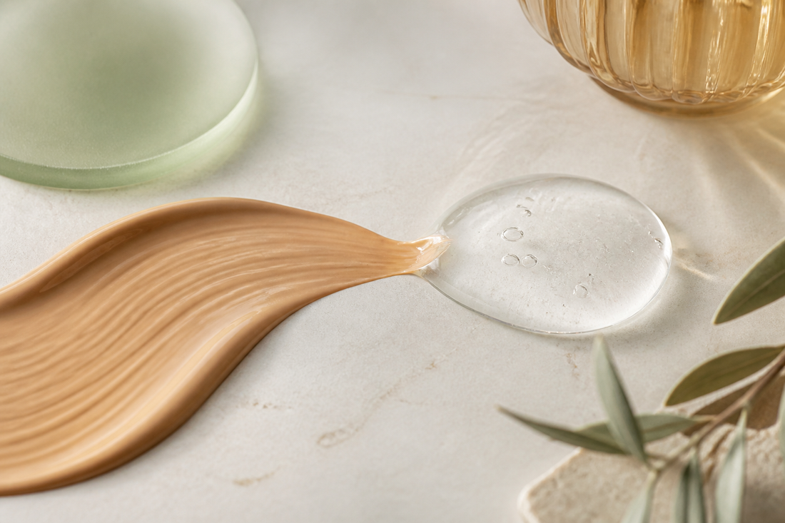 Foundation swatch meeting a clear serum droplet in a refined warm-ivory editorial scene